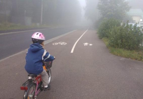 En barn cyclar på dimmig väg.