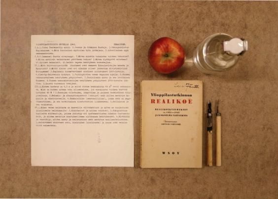 Ylioppilaan tarvikkeita vuonna 1948: reaalikoe, omena, vesipulloa ja mustekyniä.